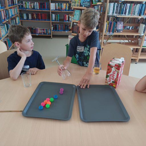 Aufgabe: Die Bälle mit dem Glas von einem Tablett auf das andere zu bringen ohne sie zu schaufeln oder schieben! 